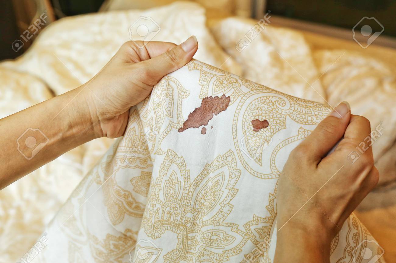 96133183 Women Hold Bed Sheet With Period Blood Spot Stains On Blur Background Need To Be Cleaning 